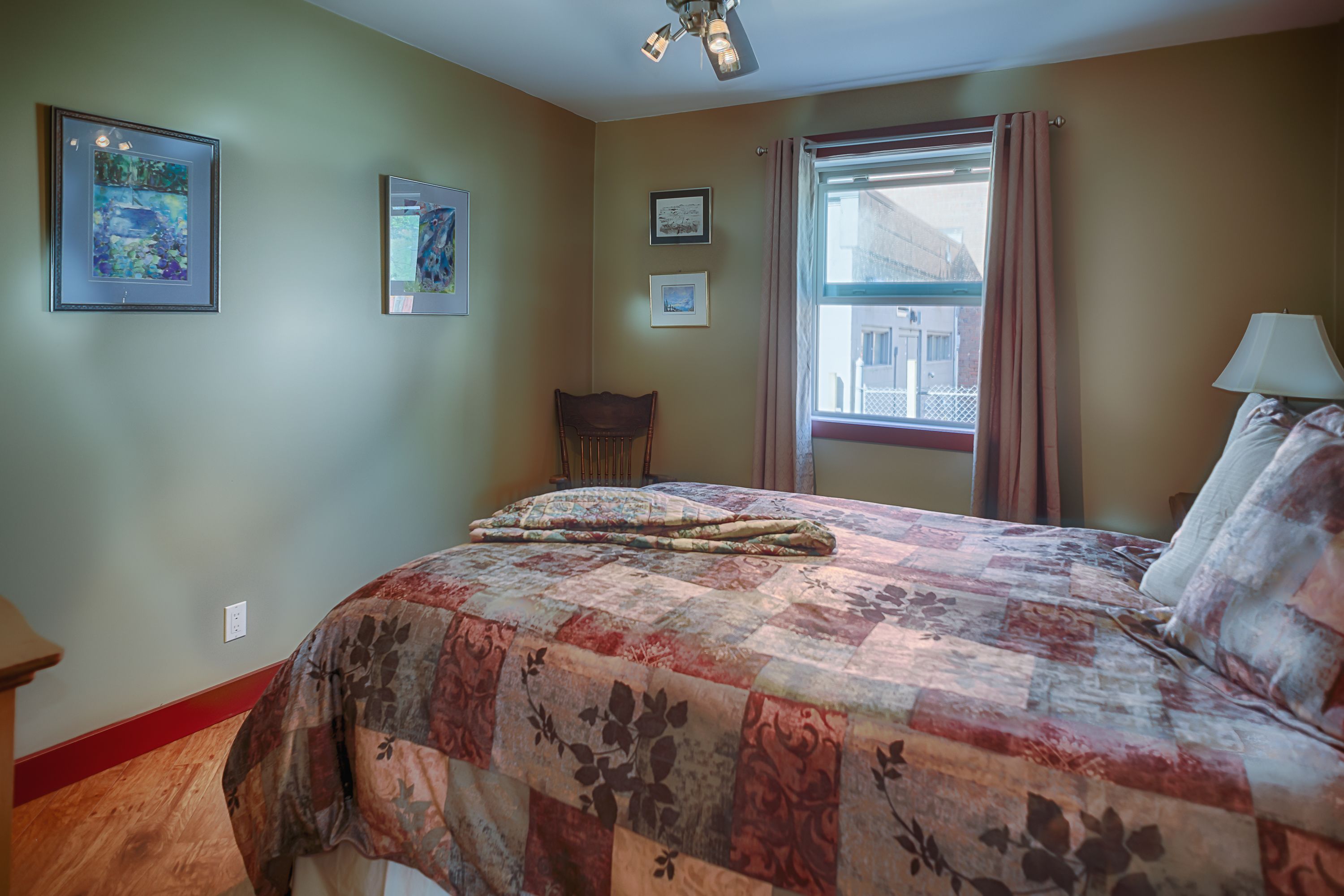 A bedroom with a large bed, a window with curtains, and framed pictures on the wall.