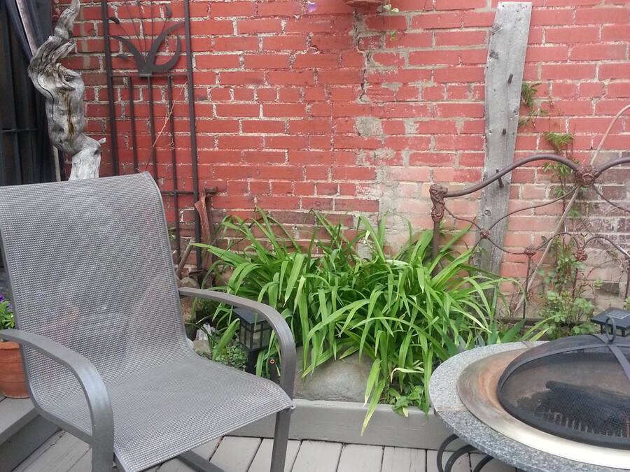 Een terras met een metalen stoel, een ronde tafel met een barbecue en een hangplanter met bloemen.