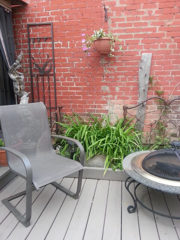 A patio with a metal chair, a round table with a grill, and a hanging planter with flowers. - Country Encounters (Coleman)