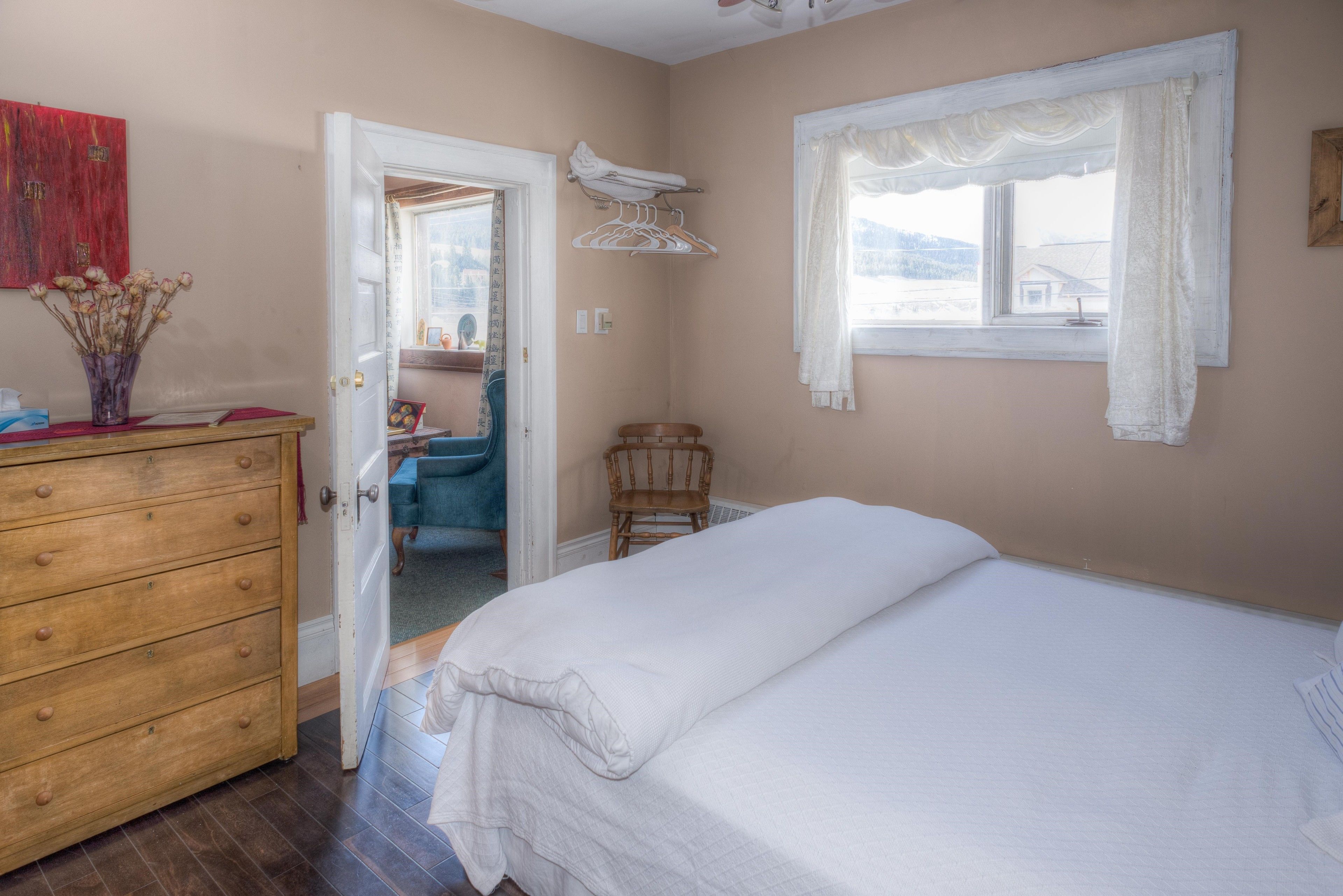 A bedroom with a bed, dresser, and a window with curtains.
