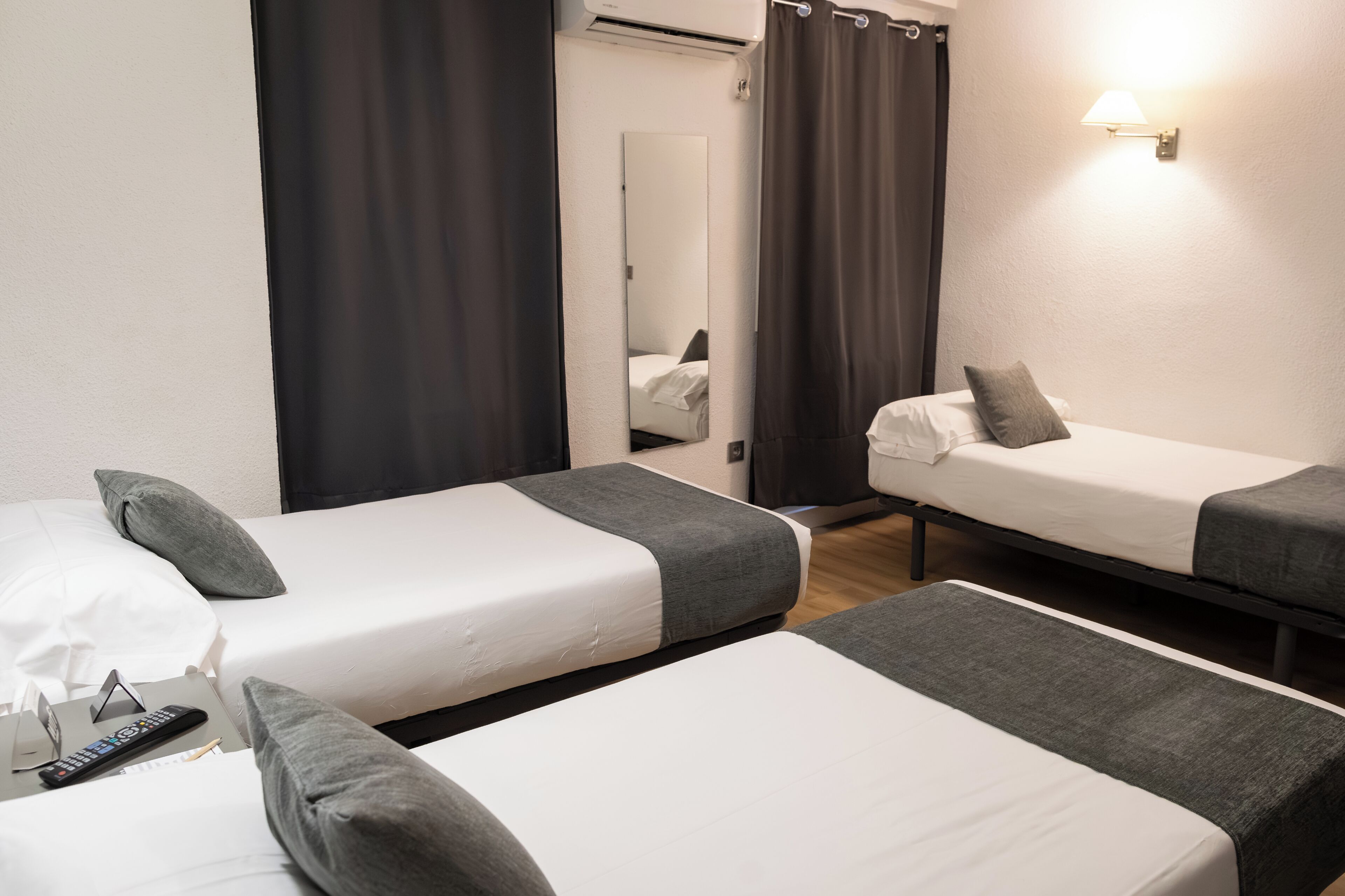 Een hotelkamer met twee eenpersoonsbedden, een spiegel, een lamp aan de muur en een afstandsbediening op het bed.
