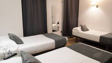 Een hotelkamer met twee eenpersoonsbedden, een spiegel, een lamp aan de muur en een afstandsbediening op het bed.