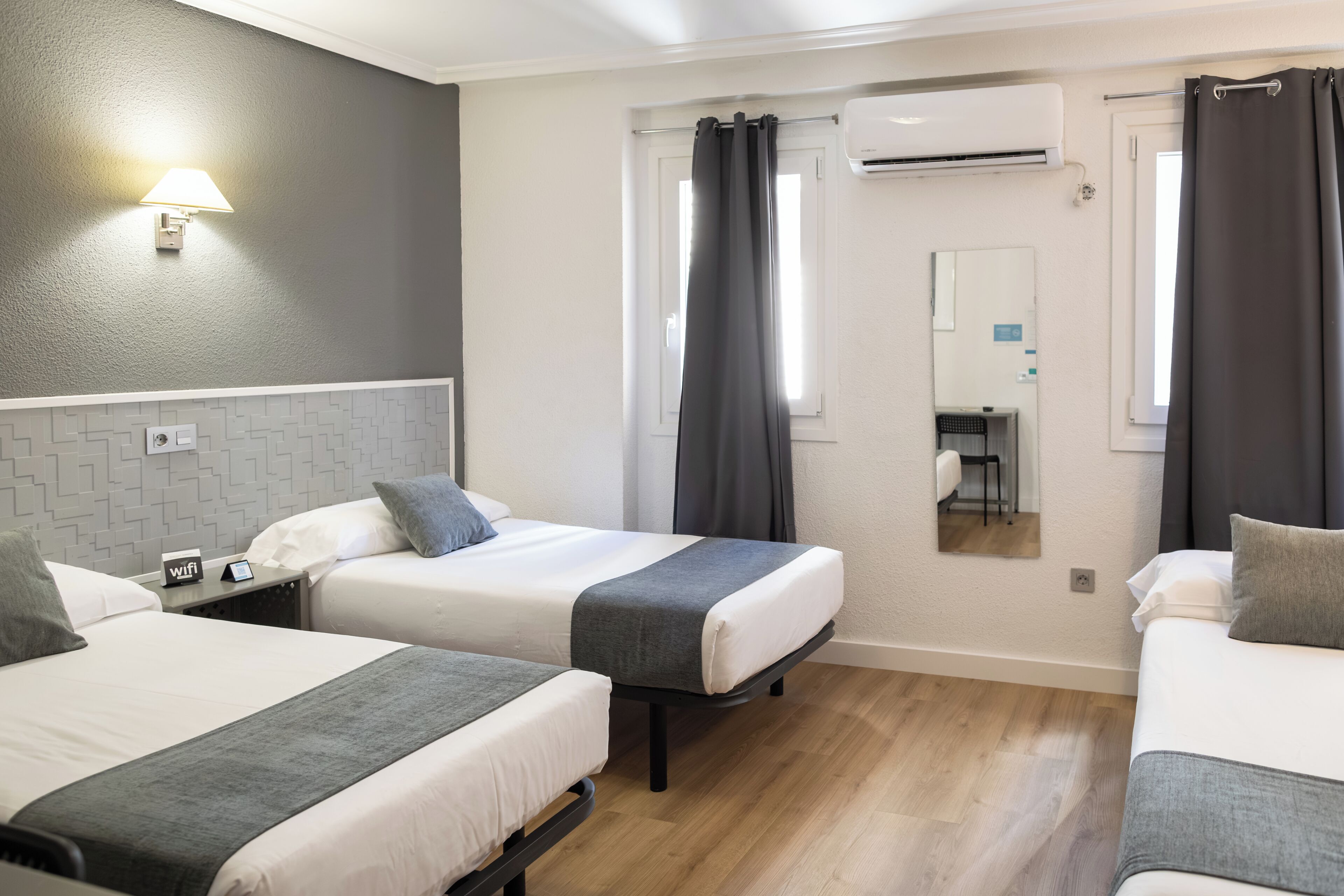 Habitación de hotel con dos camas, una mesita con un teléfono, una lámpara de pared y un equipo de aire acondicionado.
