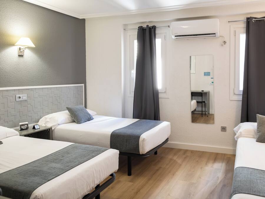 Habitación de hotel con dos camas, una mesita con un teléfono, una lámpara de pared y un equipo de aire acondicionado.