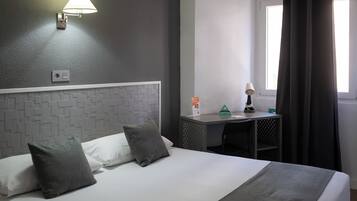 A hotel room with a bed, a desk, a lamp, and a window with curtains.