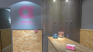 Zona de recepción con mostrador de madera, un cartel en la pared de 'alda hotels' que destaca 'el mejor precio, ubicación y servicio', y un casillero con un letrero de Wi-Fi.