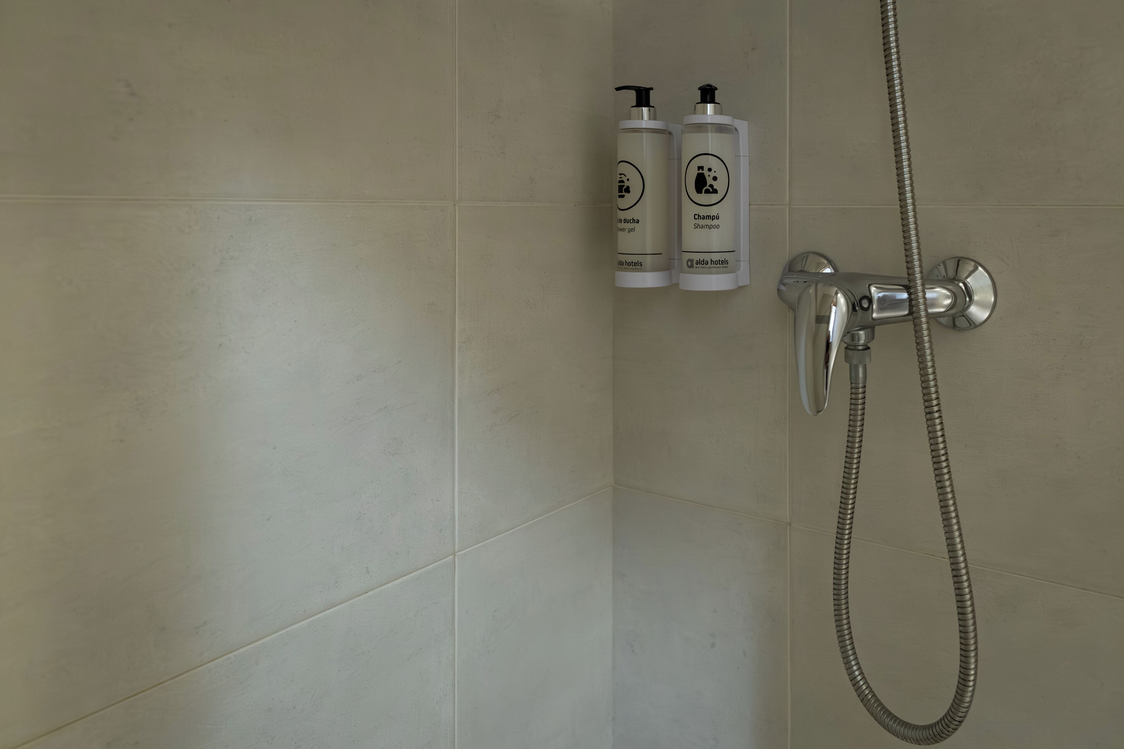 A bathroom with a shower, two shampoo bottles, and a handheld showerhead.