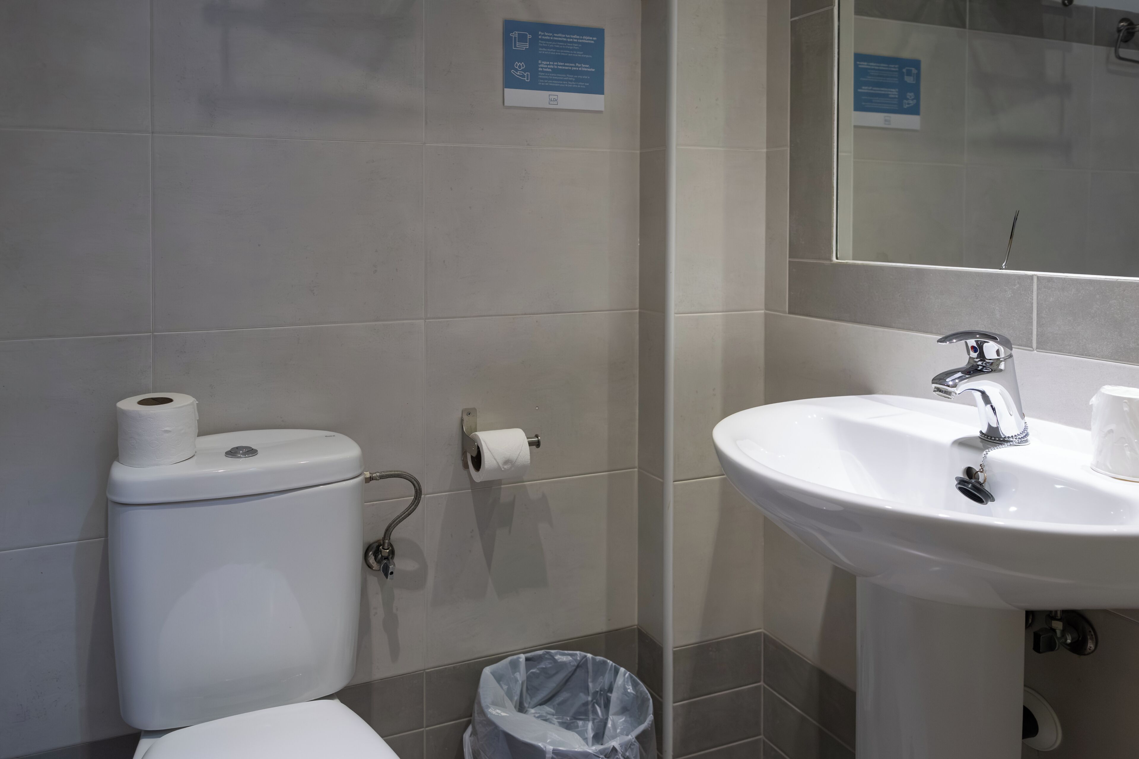 A bathroom with a toilet, a sink, and a trash bin.