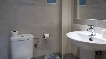 A bathroom with a toilet, a sink, and a trash bin.