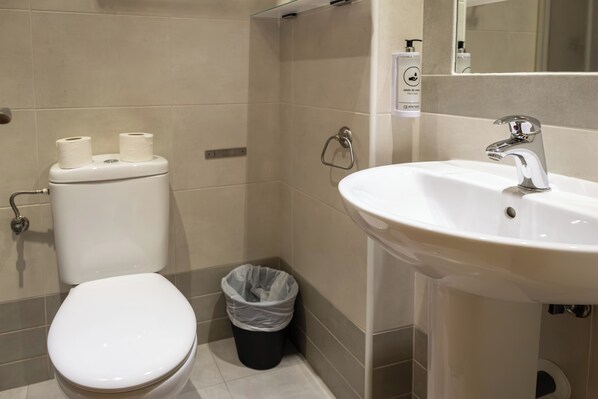 Baño con inodoro, bidé, lavamanos y un cubo de basura.