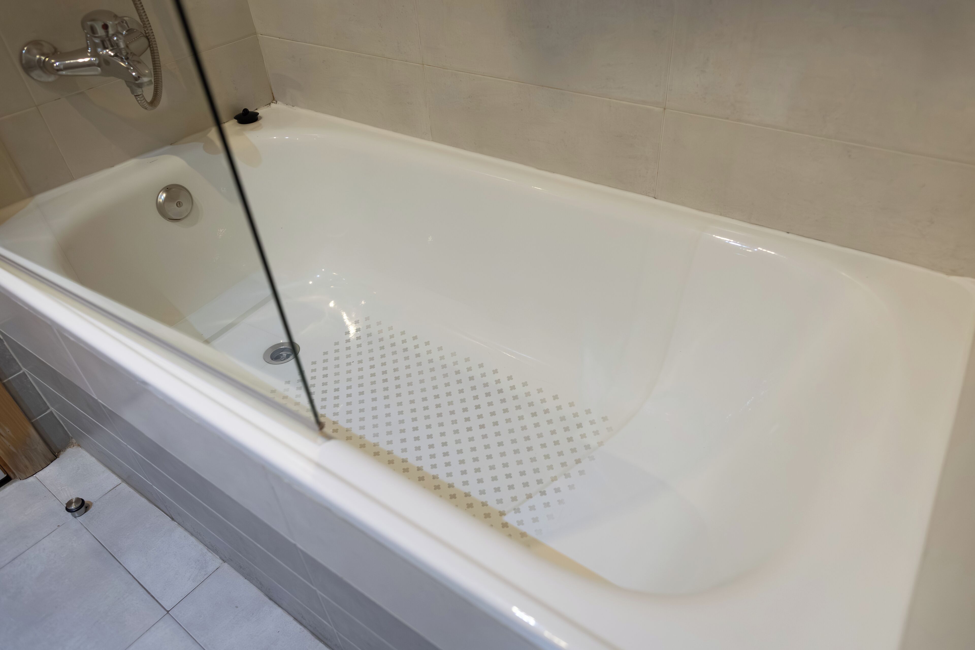 Una bañera con ducha, desagüe y rejilla perforada.