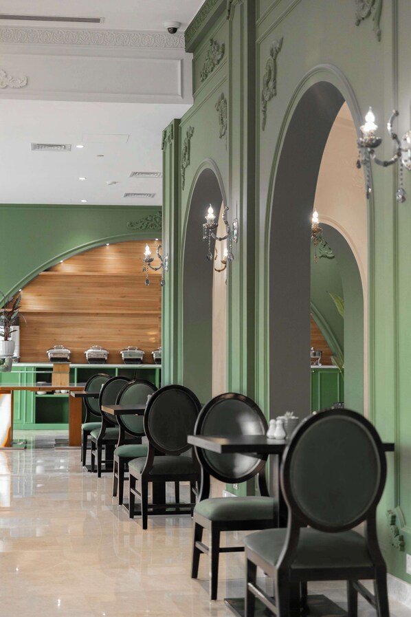 A restaurant with green walls, arched doorways, and rows of black chairs.
