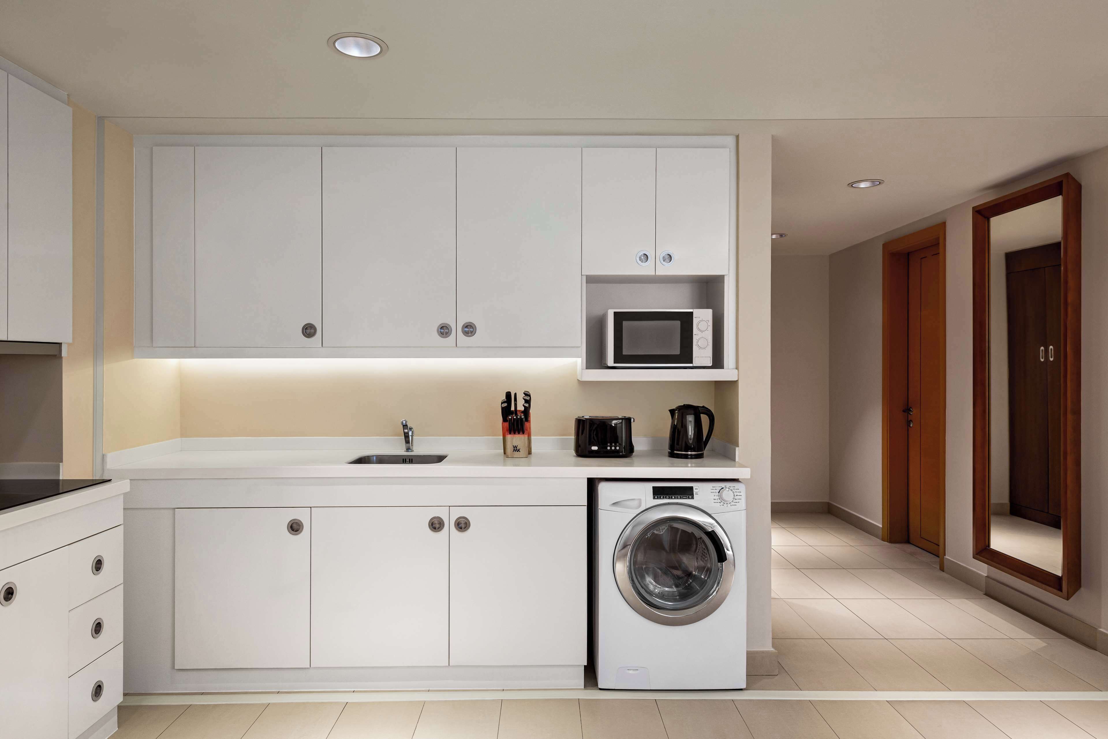 A modern kitchen with white cabinetry, a built-in microwave, a coffee maker, and a washing machine.