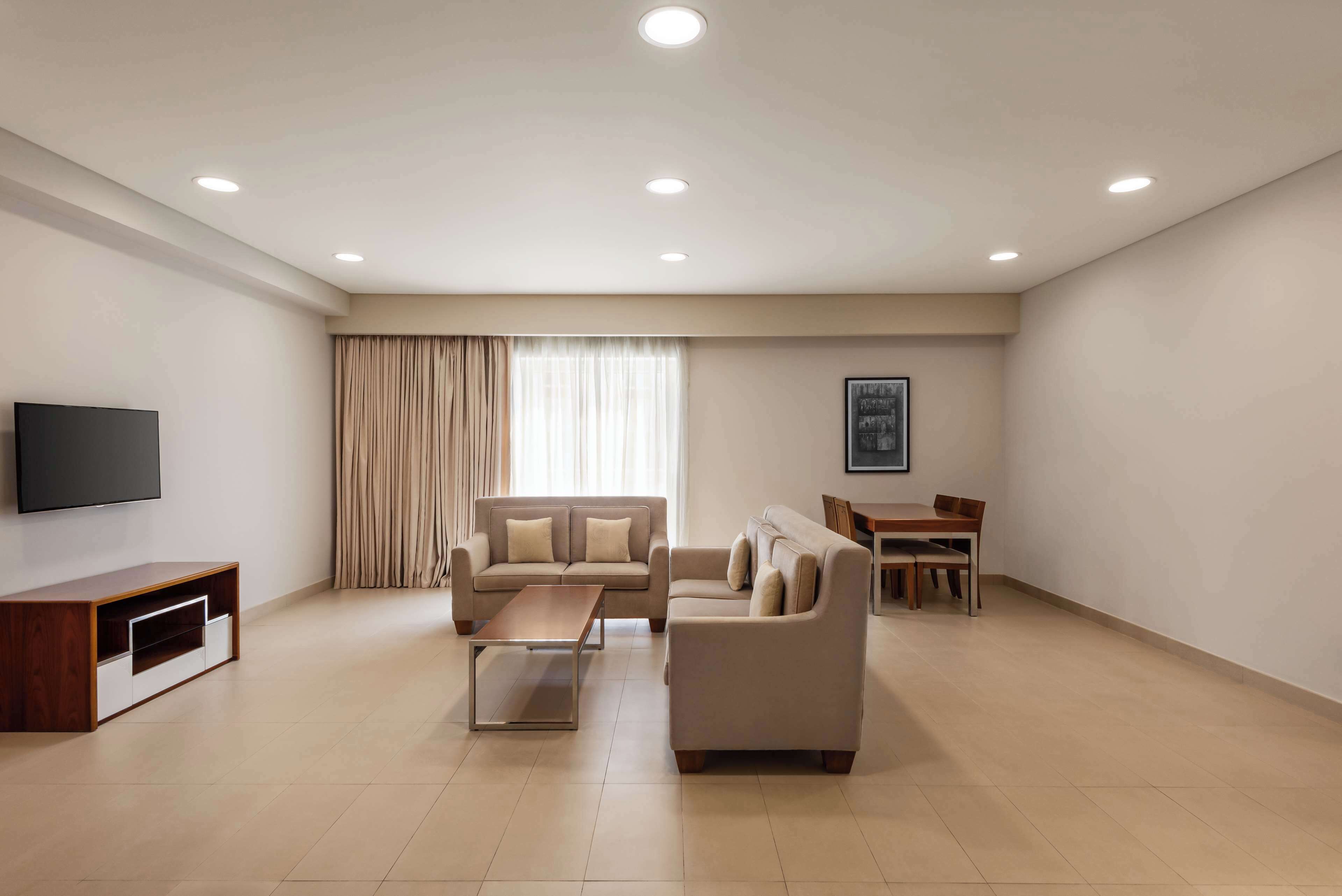 A modern living room with a sofa, coffee table, TV, and a dining area with chairs and a table.