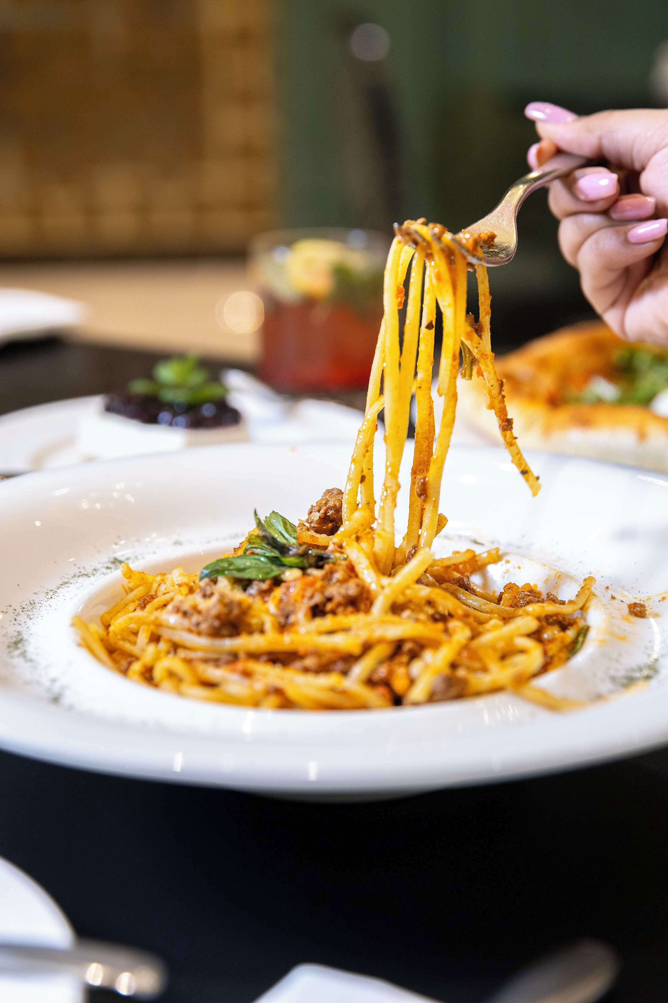 A plate of spaghetti with meat sauce and a garnish, being lifted by a fork.