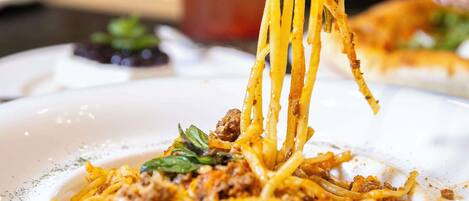 A plate of spaghetti with meat sauce and a garnish, being lifted by a fork.