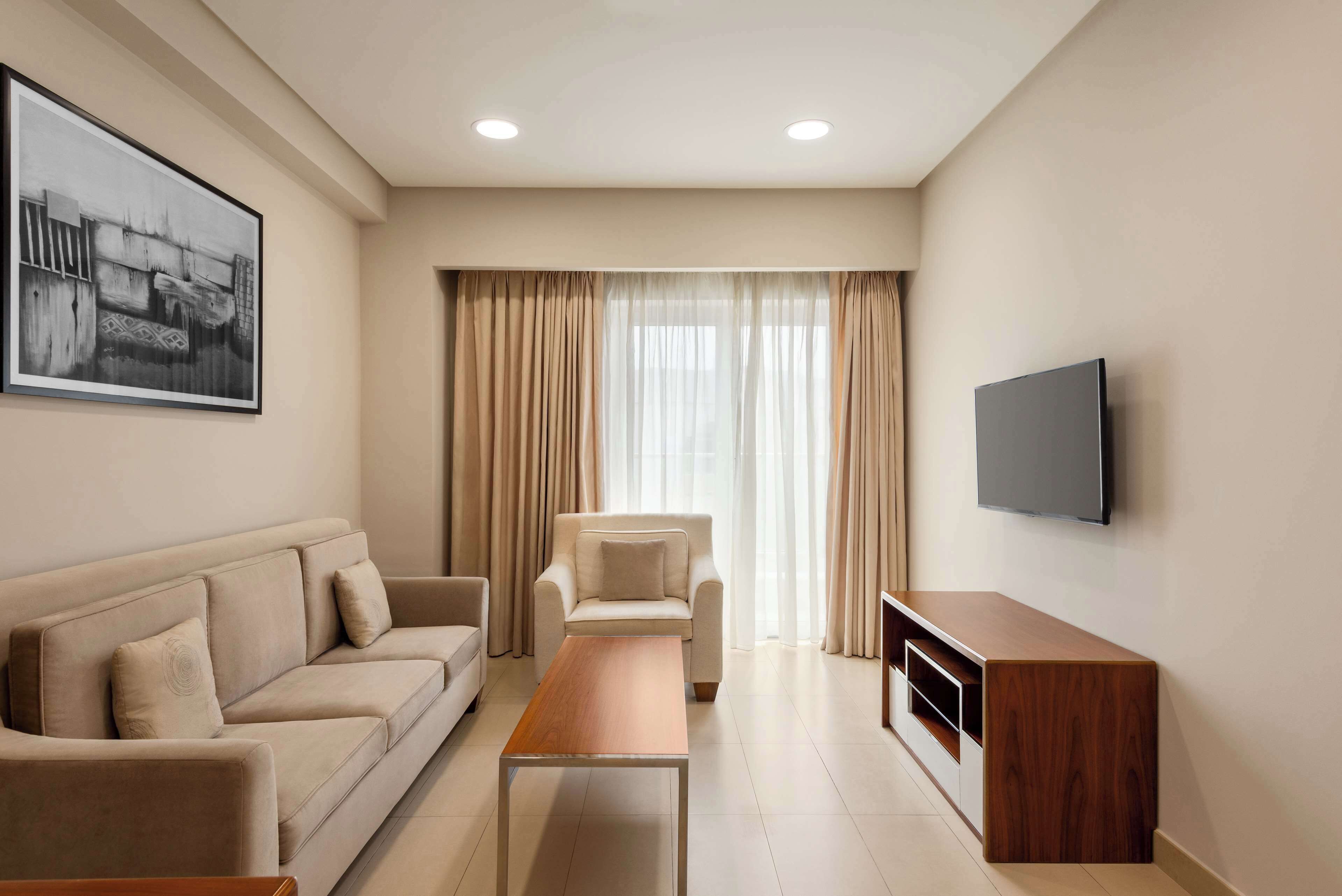 A modern living room with a sofa, a coffee table, a TV, and a large window with curtains.
