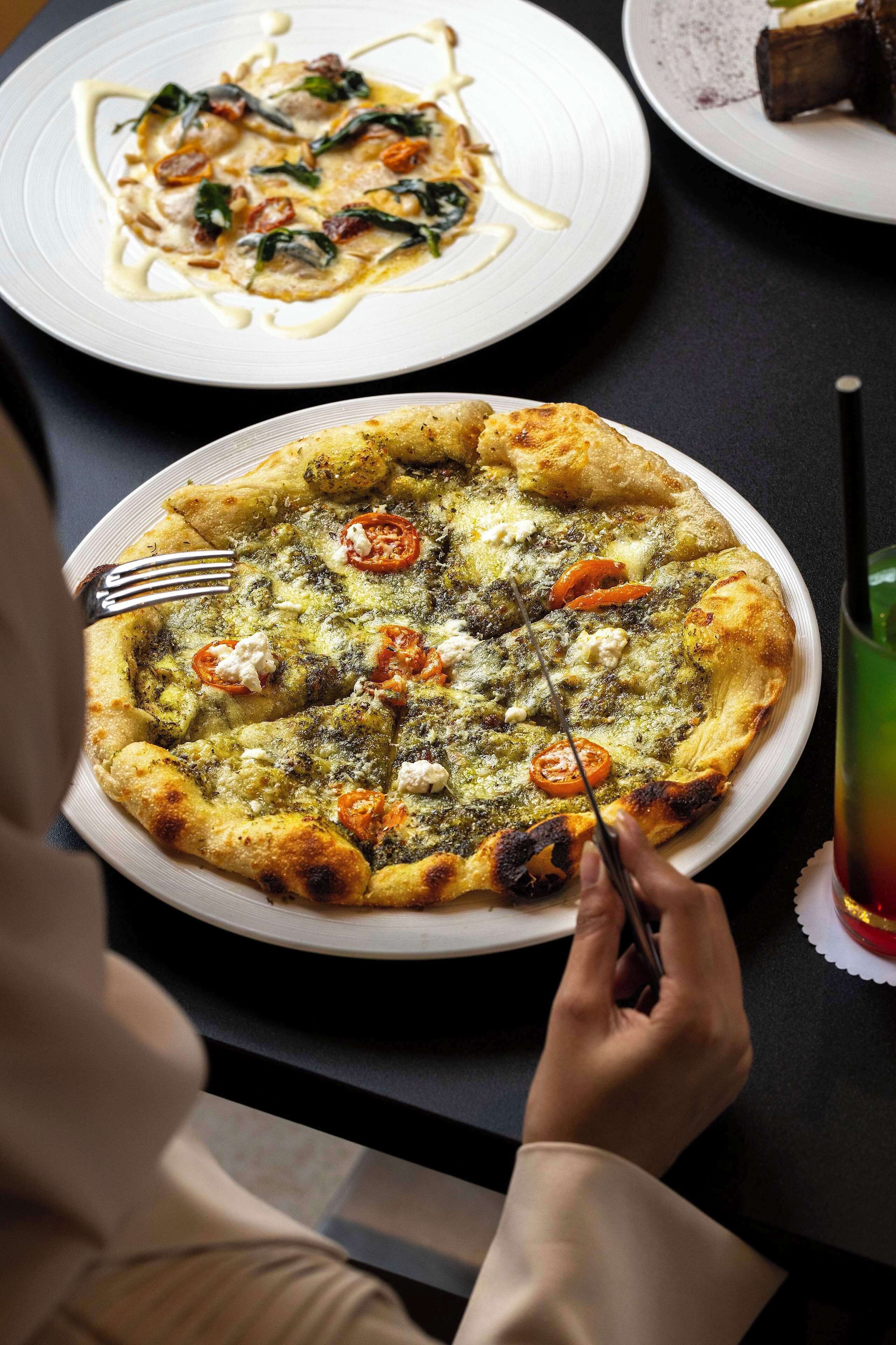 Una persona cortando una pizza con tenedor y cuchillo en un plato.