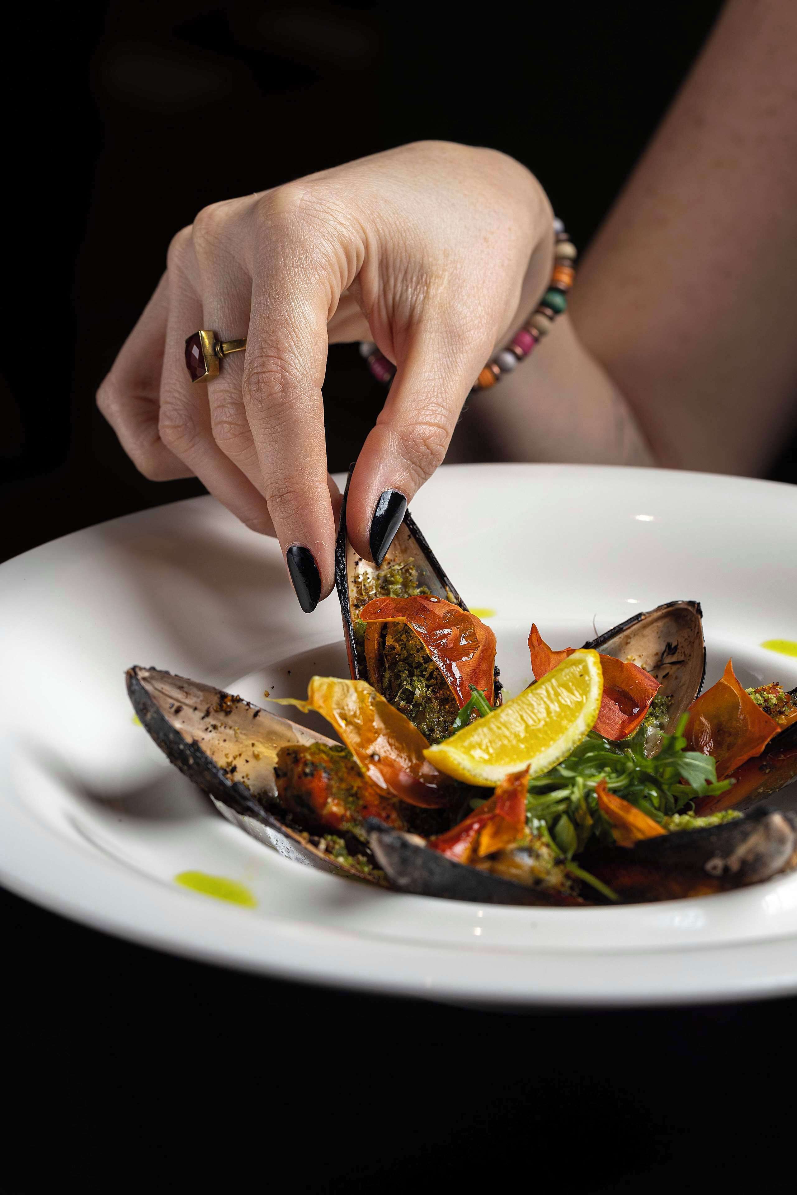 Una mano che tiene una forchetta e taglia un piatto di cozze su un piatto bianco.