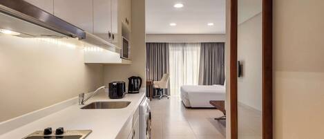 A modern hotel room with a kitchenette, a bed, a chair, and a large mirror.