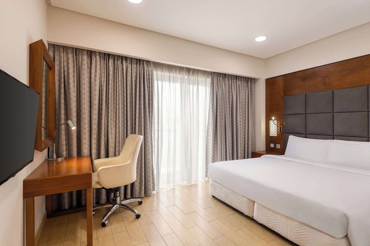 Une chambre d’hôtel avec un lit, un bureau et une chaise, une télévision et une fenêtre avec des rideaux.