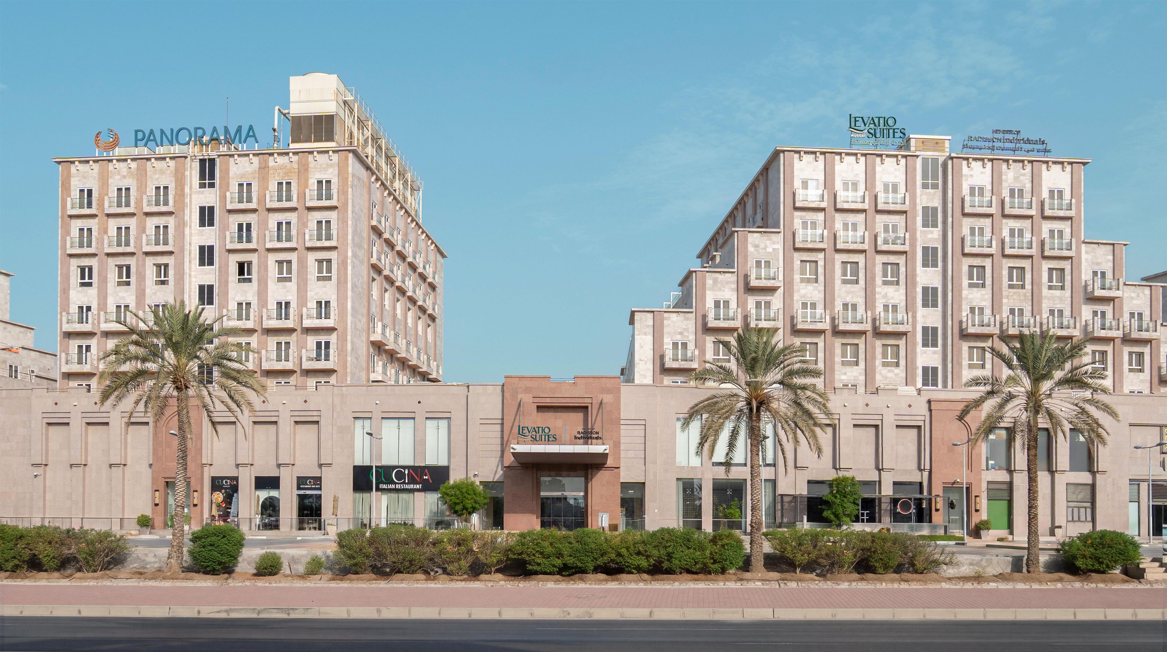 Un hotel de varios pisos con balcones, un restaurante y palmeras.