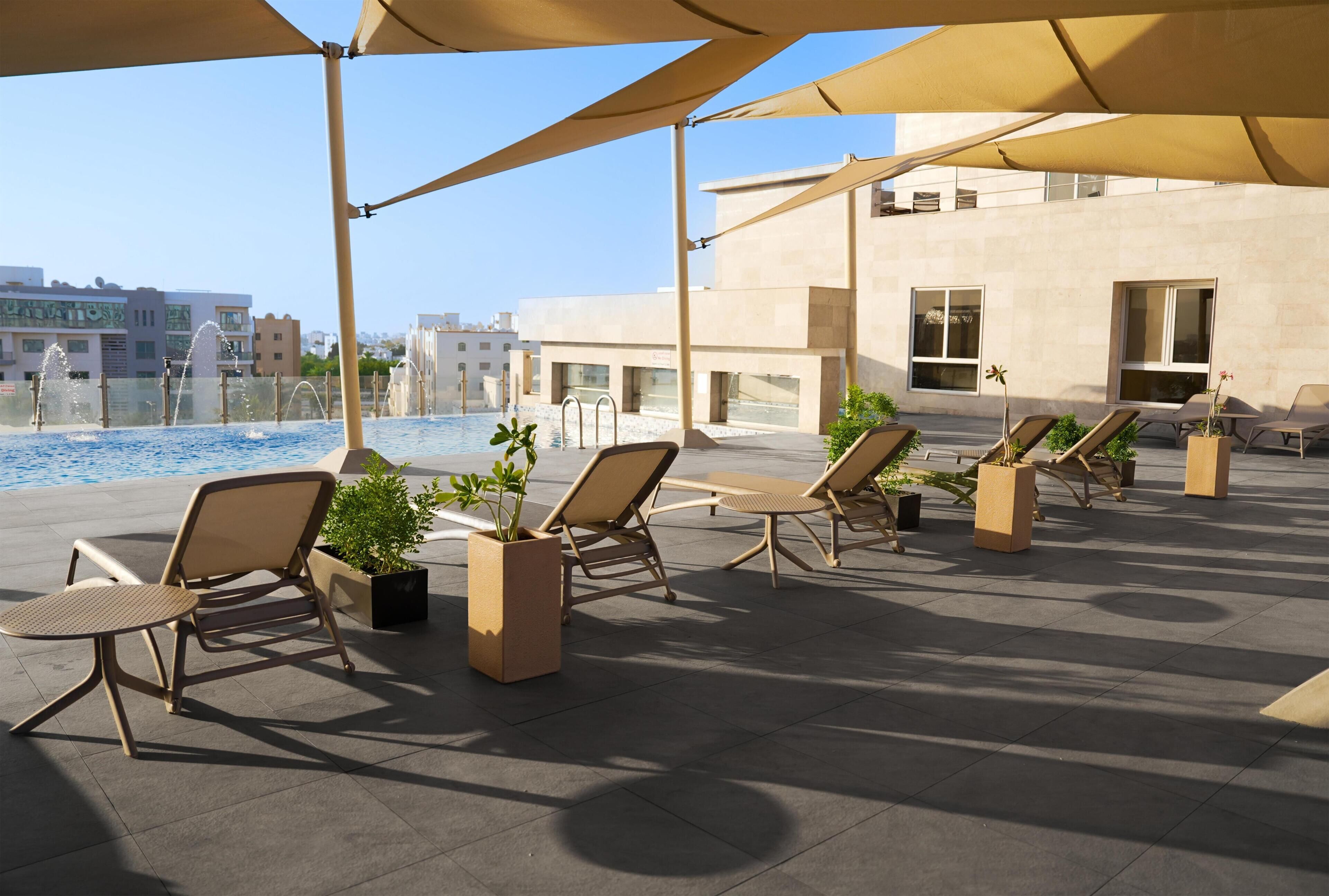 A rooftop pool area with lounge chairs and umbrellas, a clear view of the pool, and a modern building in the background.