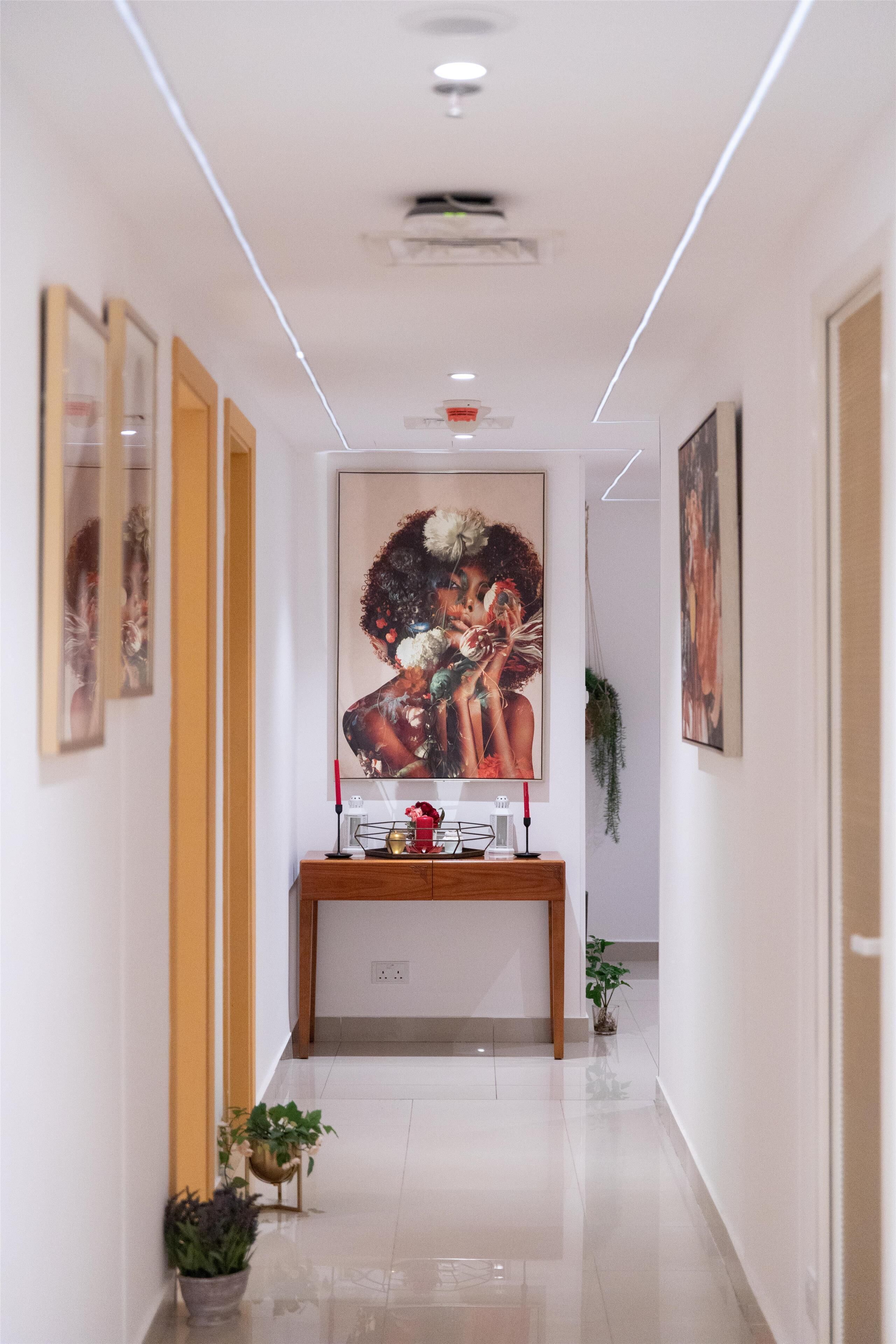 Un couloir avec une console en bois, des œuvres d’art encadrées et des plantes en pot.