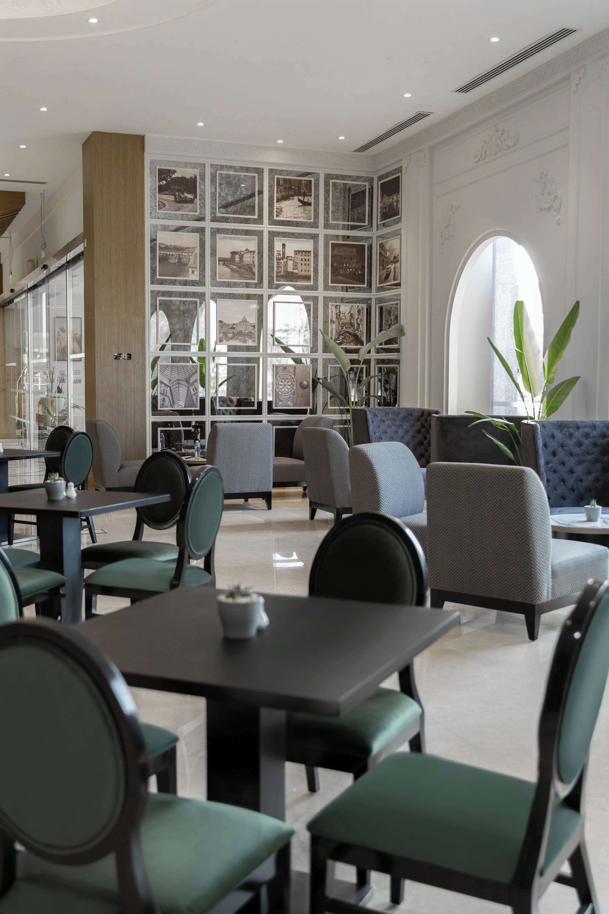 Un interior moderno con una zona de estar que incluye sofás y sillones, una pared decorada con cuadros enmarcados y un ventanal con una planta.