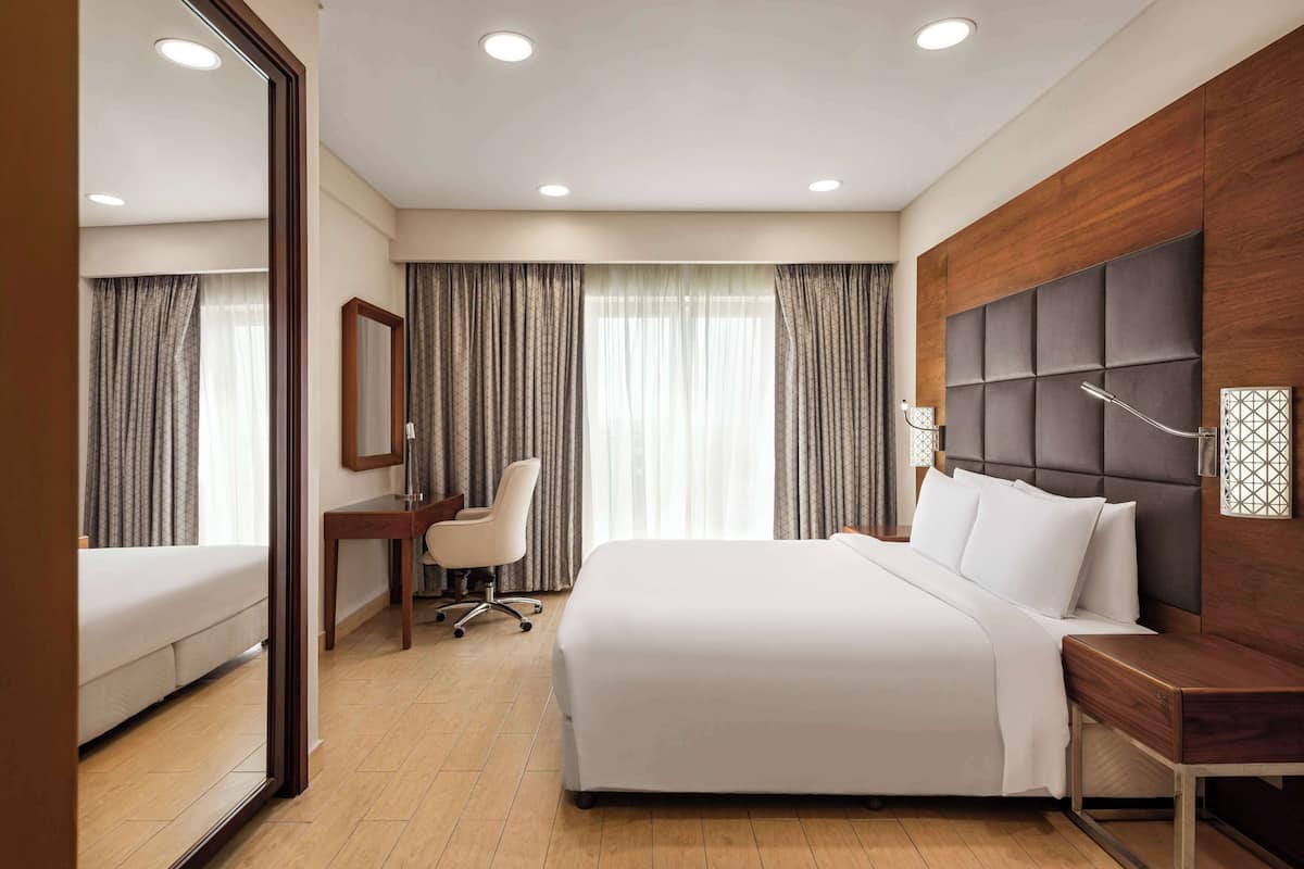 Une chambre d’hôtel avec un grand lit, un bureau, une chaise et un miroir.