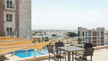 A rooftop terrace with a pool, outdoor seating, and a view of the cityscape.