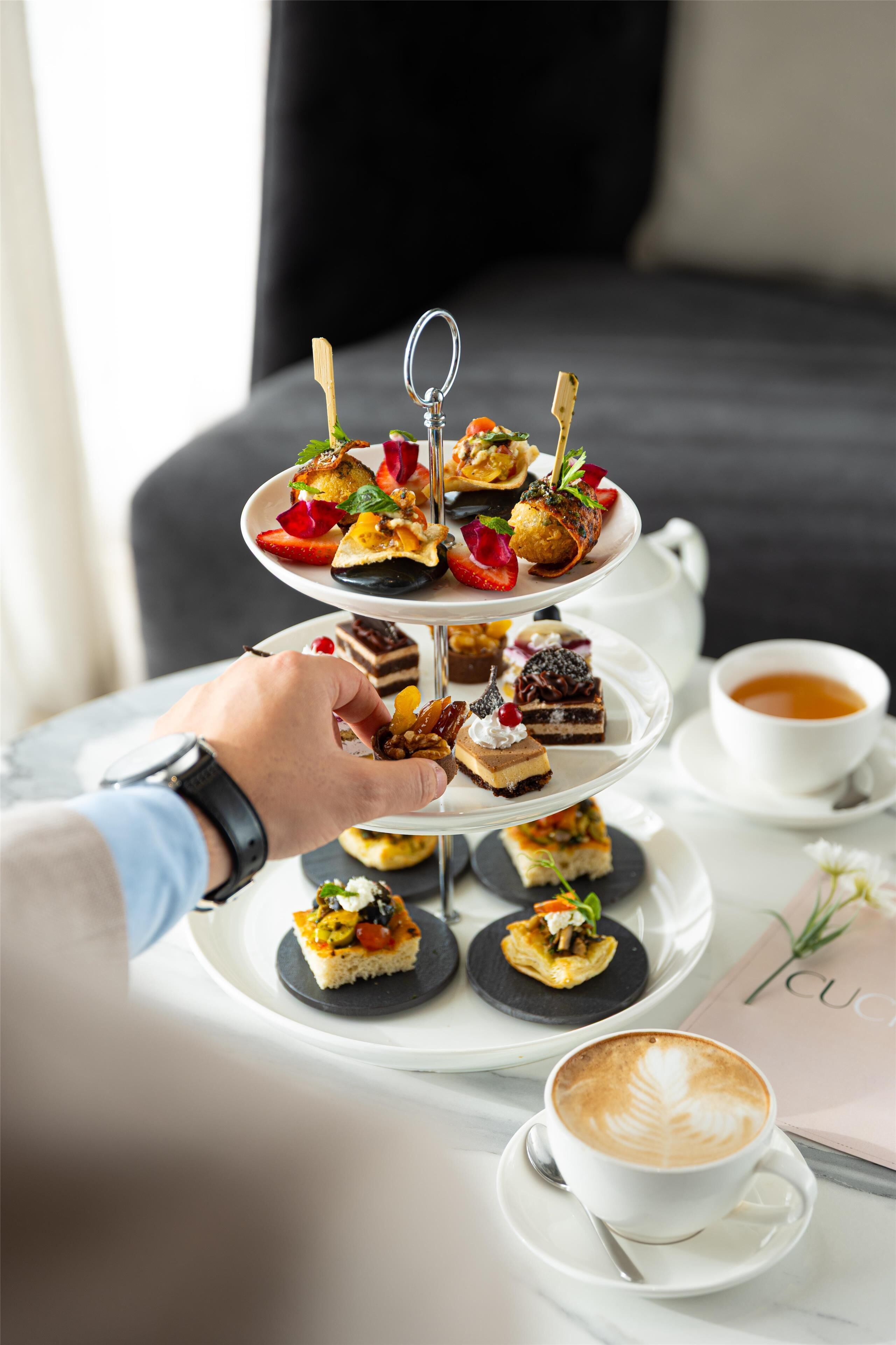 A three-tiered dessert tray with various pastries and a cup of coffee on a table.