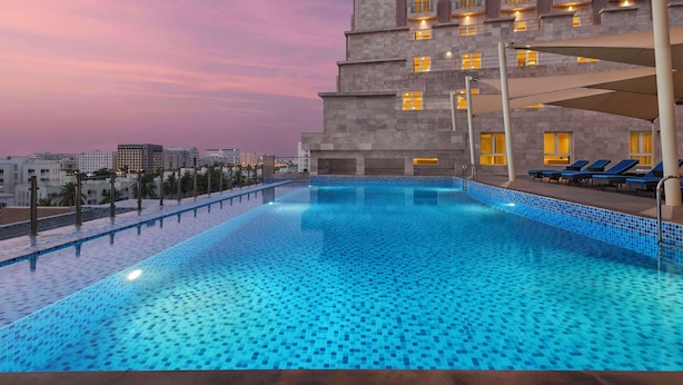 Piscina com borda revestida, ao lado de um edifício com várias varandas e janelas, e vista para o horizonte urbano ao fundo.