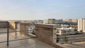 Terraço no telhado com guarda-corrimão de metal, piso de concreto e vista para um horizonte urbano com edifícios e palmeiras.