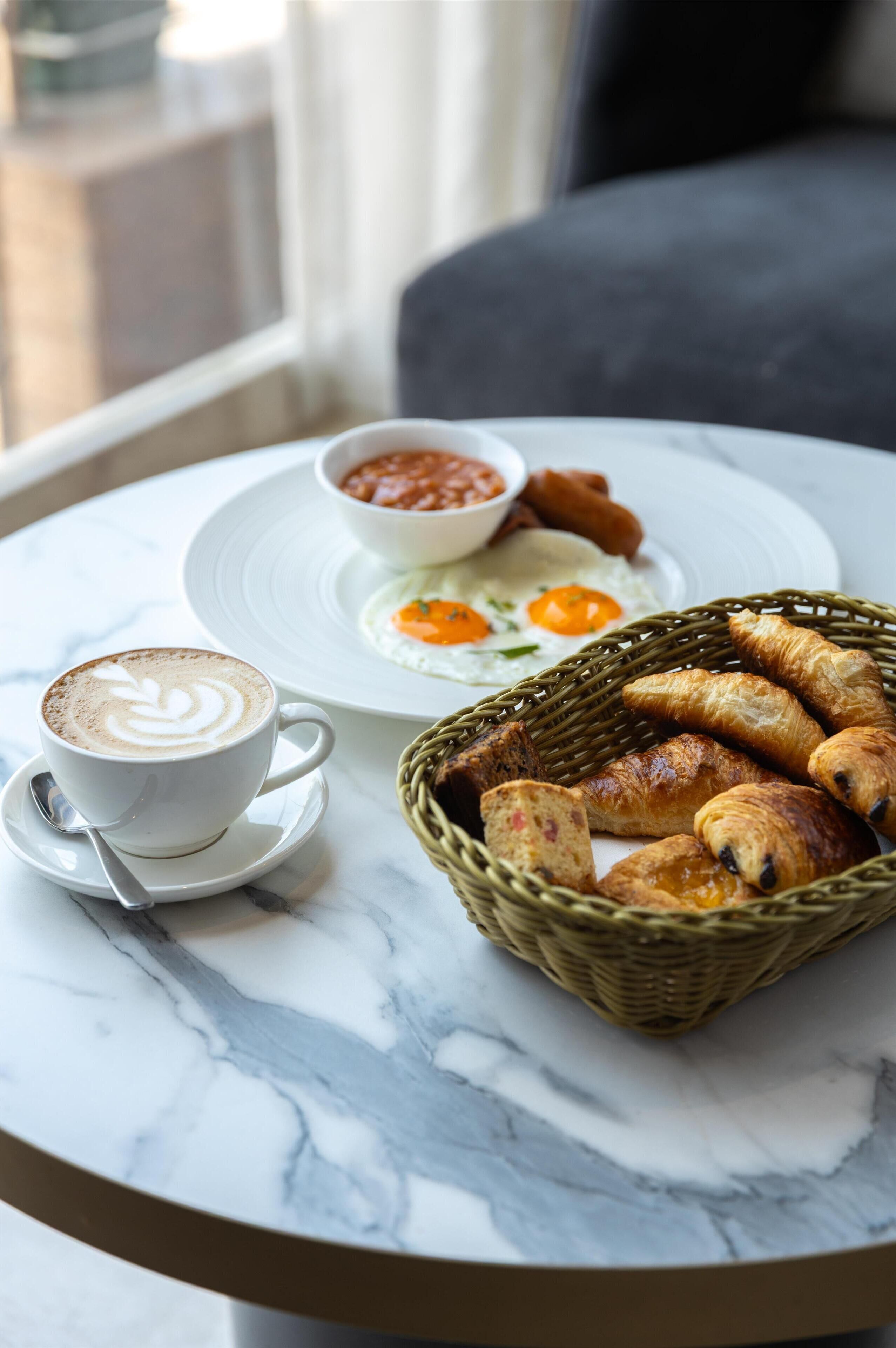 Ein Frühstückstisch mit einer Kaffeetasse, einem Teller mit Eiern und Croissants sowie einer Schale Suppe auf einer Marmortafel.
