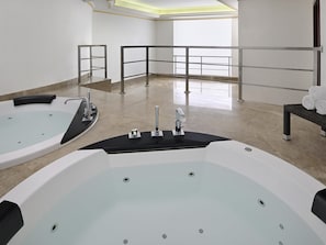 A spa room with two large tubs, a bench with towels, and a view of the outside through a window. - Mövenpick Hotel City Star Jeddah (Jeddah)