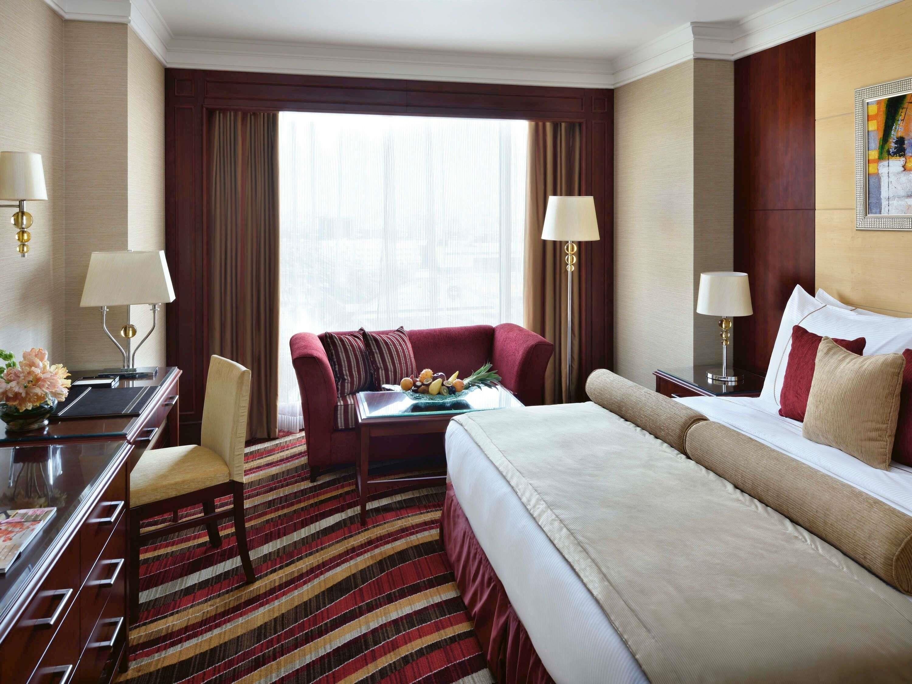 Ein Hotelzimmer mit einem Bett, einem Schreibtisch, einem Sessel, einer Couch und einem Esstisch mit Früchten.