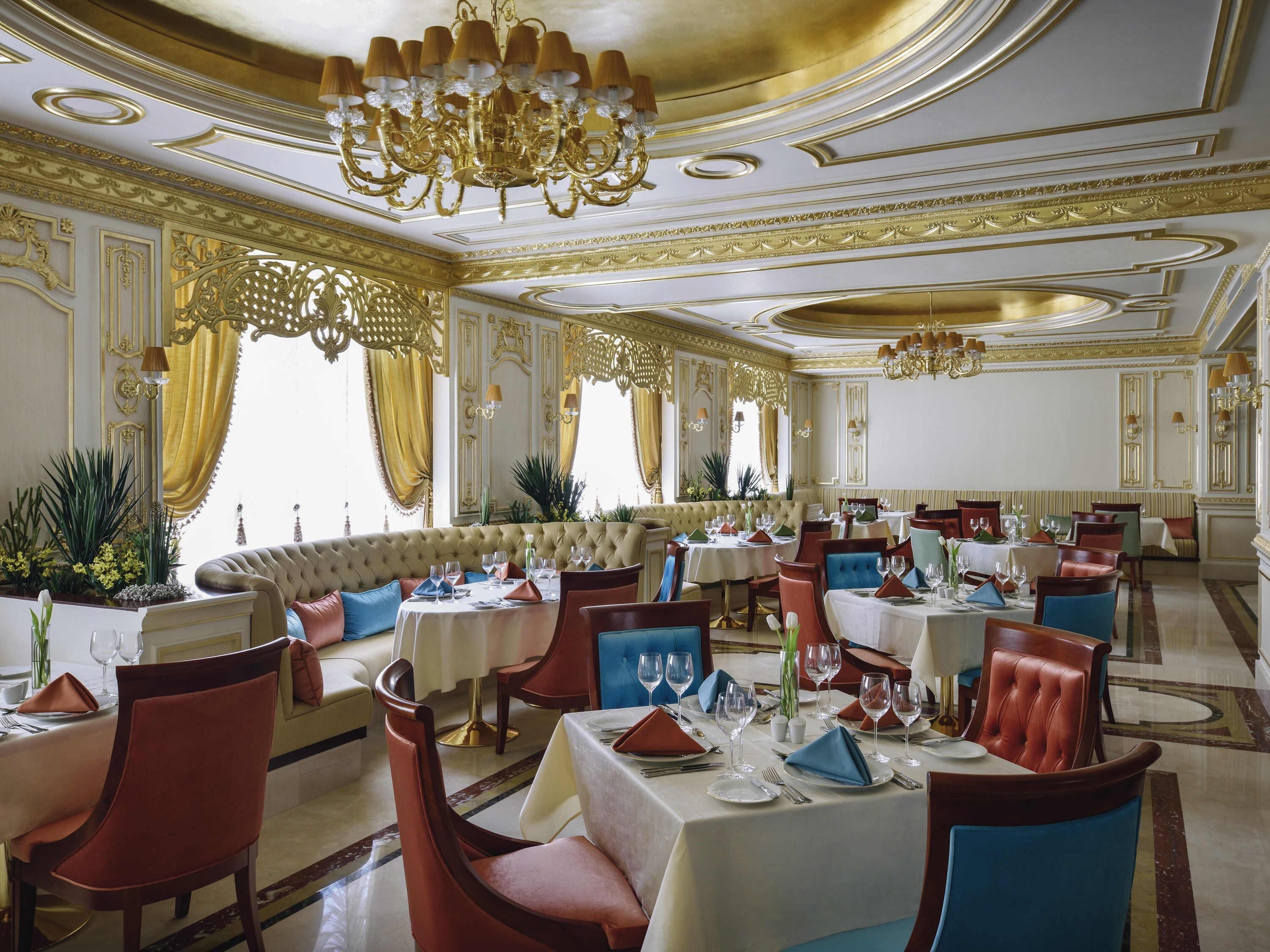 A luxurious dining room with ornate chandeliers, plush seating, and elegant table settings.