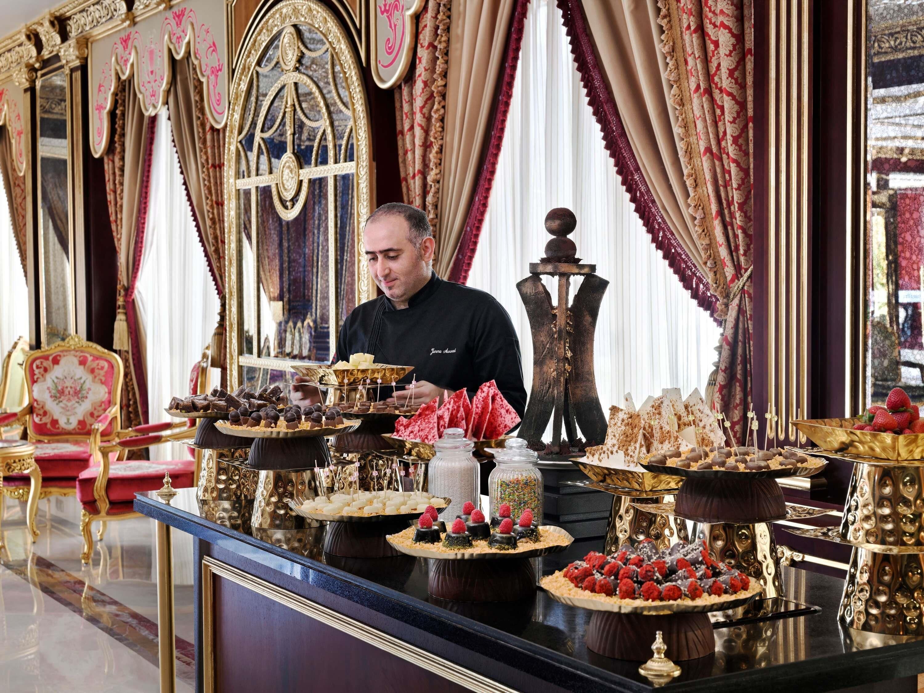 A luxurious setting with ornate furniture and a variety of desserts displayed on a reflective black surface.