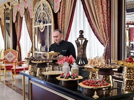Eine luxuriöse Umgebung mit kunstvollen Möbeln und einer Auswahl an Desserts, die auf einer glänzenden schwarzen Oberfläche präsentiert werden.