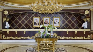 Zona de recepción con un candelabro dorado, mostrador de recepción, retratos enmarcados y una mesa decorativa con jarrones.