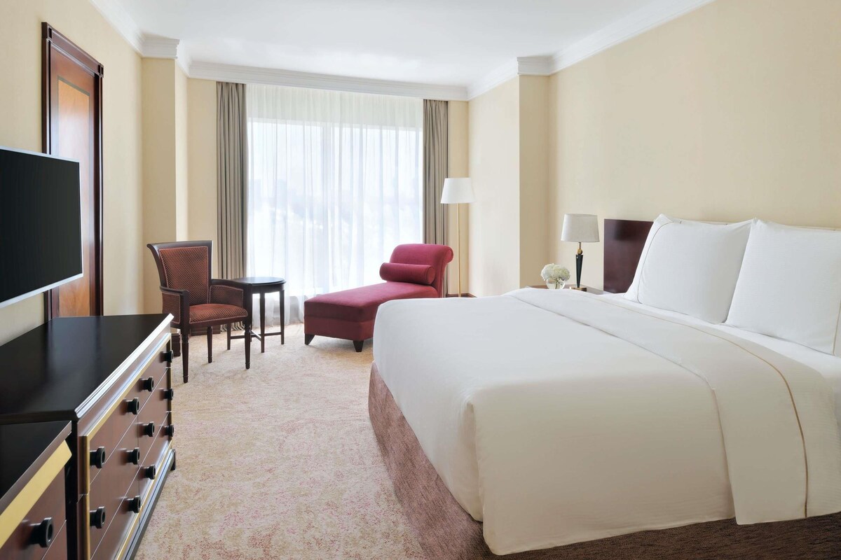 Habitación de hotel con cama, televisor, escritorio y silla, y ventana con cortinas.