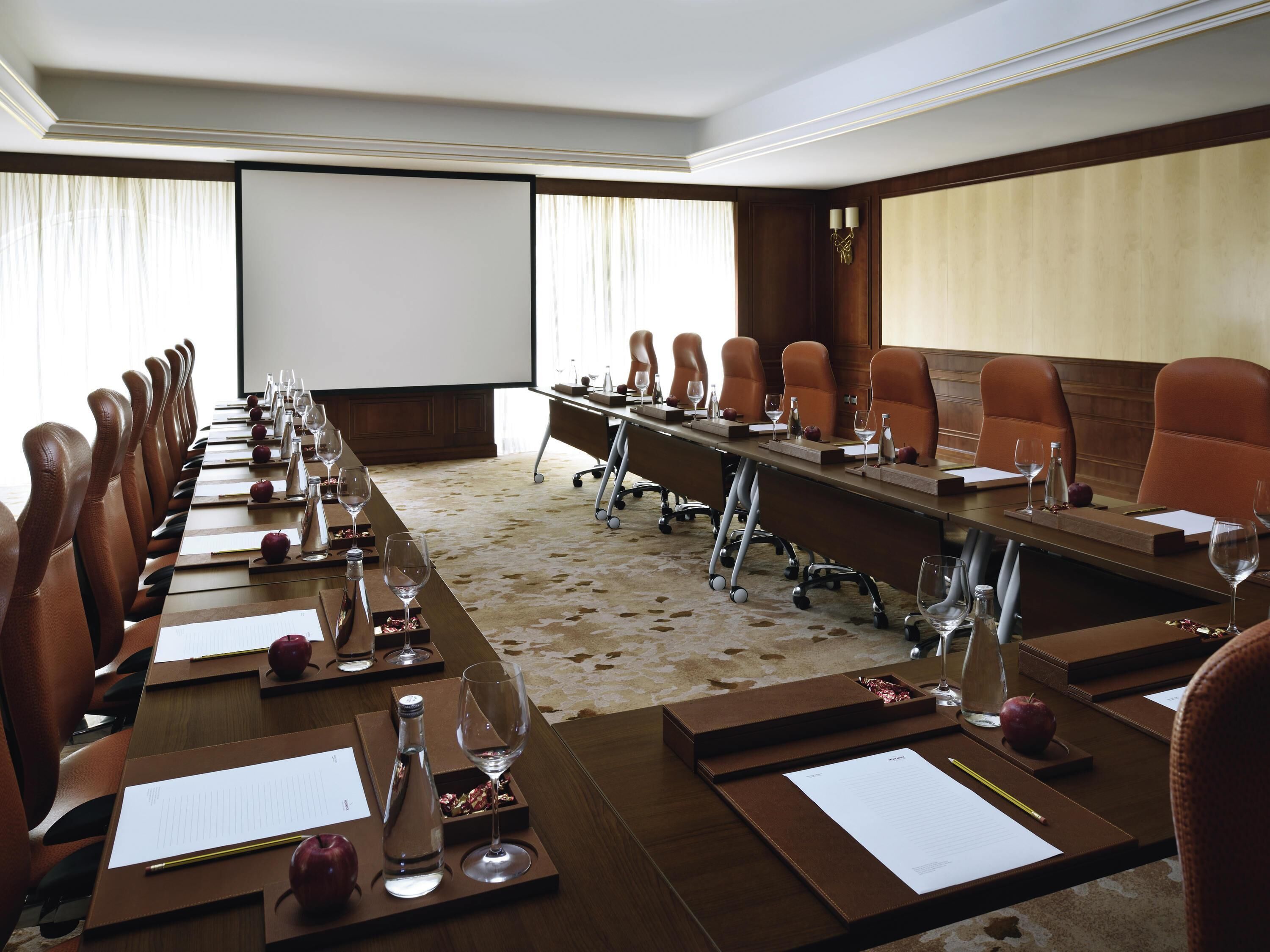 A conference room with a long table, chairs, a projector screen, and a carpeted floor.