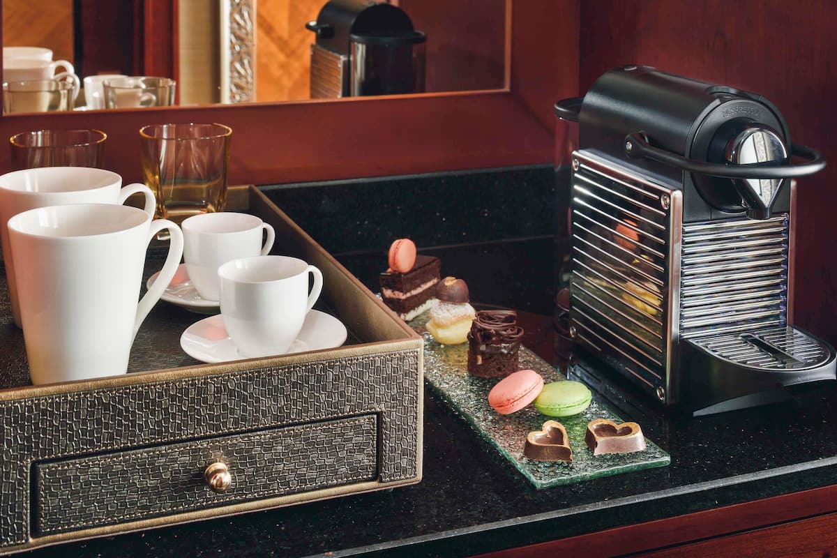 Una cafetera, tazas blancas, una bandeja con postres y una caja texturizada sobre una encimera.