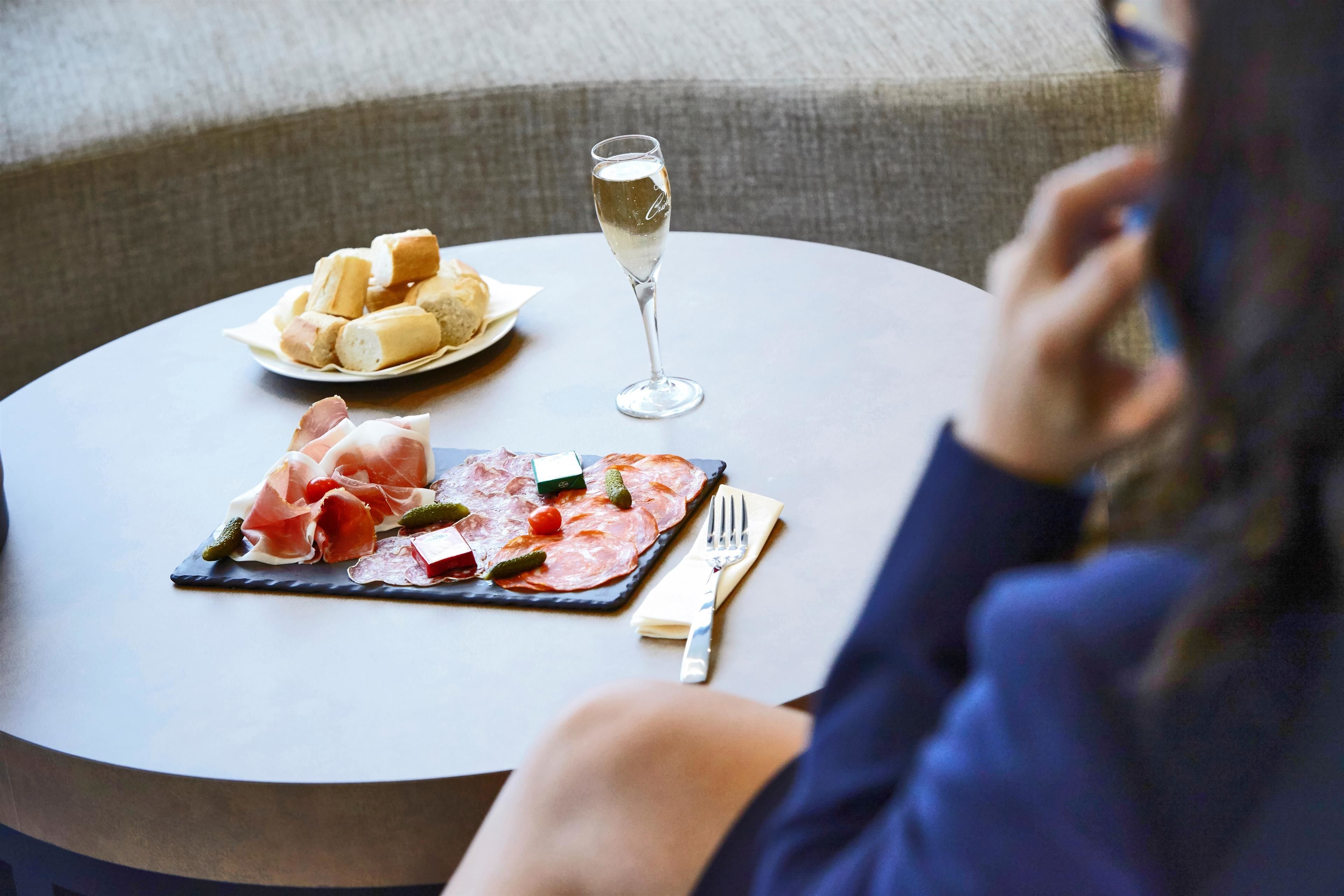 Une table ronde avec une assiette de charcuteries et de fromages, un verre de vin blanc et une fourchette.