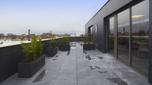 Una terraza moderna en la azotea con plantas en macetas, un muro de cristal y vistas a la ciudad.