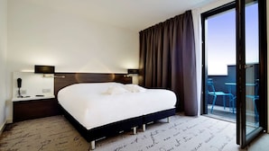 Una habitación de hotel moderna con una cama grande, una mesita de noche con teléfono y vistas al balcón exterior.