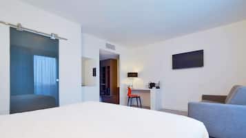A hotel room with a large bed, a desk with a chair, a TV on the wall, and a wardrobe.