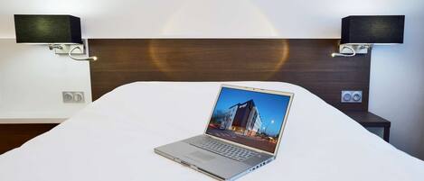 Quarto de hotel com cama, um laptop sobre a cama e dois alto-falantes fixados na parede.