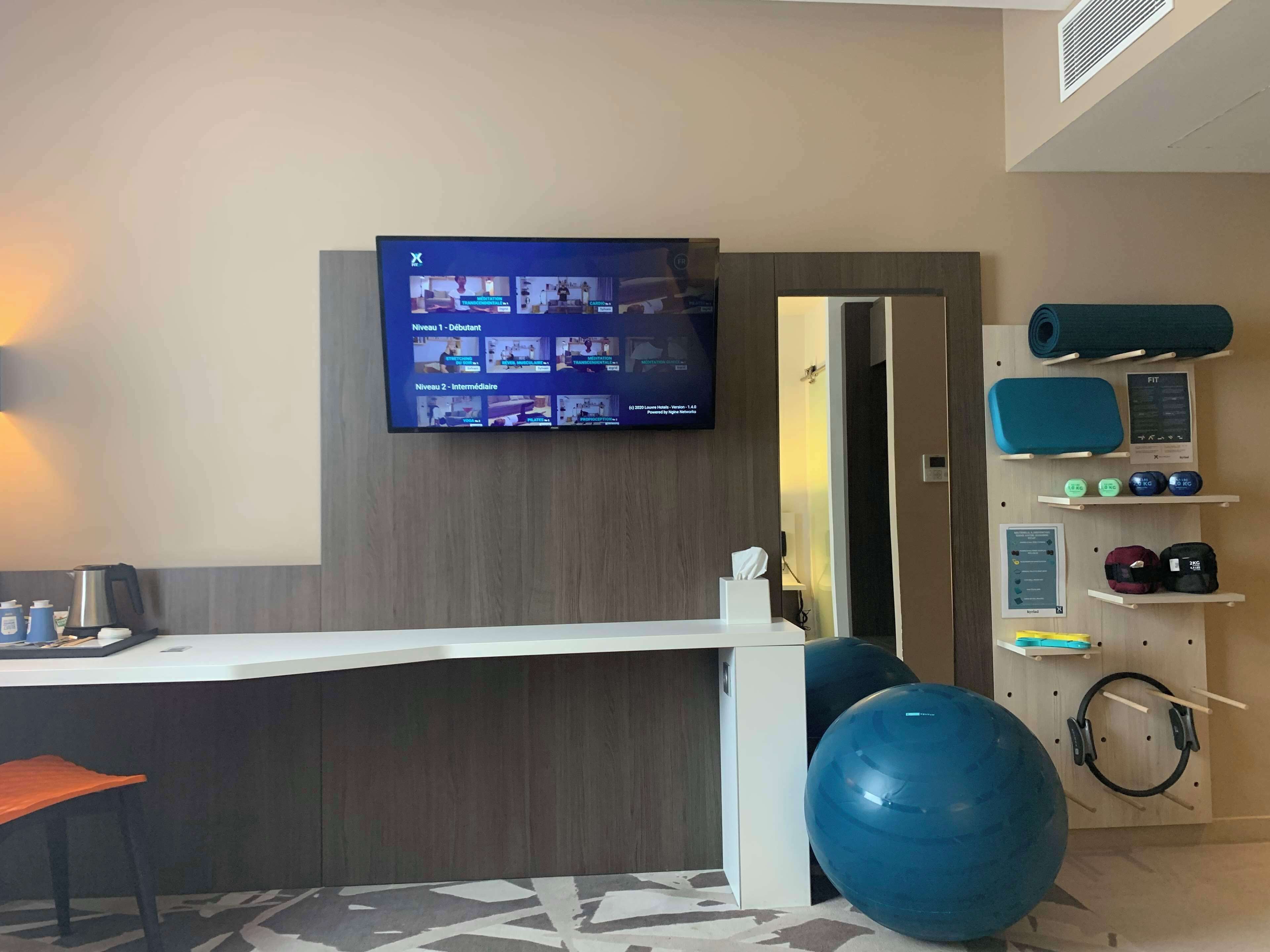 Un gimnasio con equipo de ejercicio, una televisión mostrando videos de entrenamiento y un mostrador de recepción.